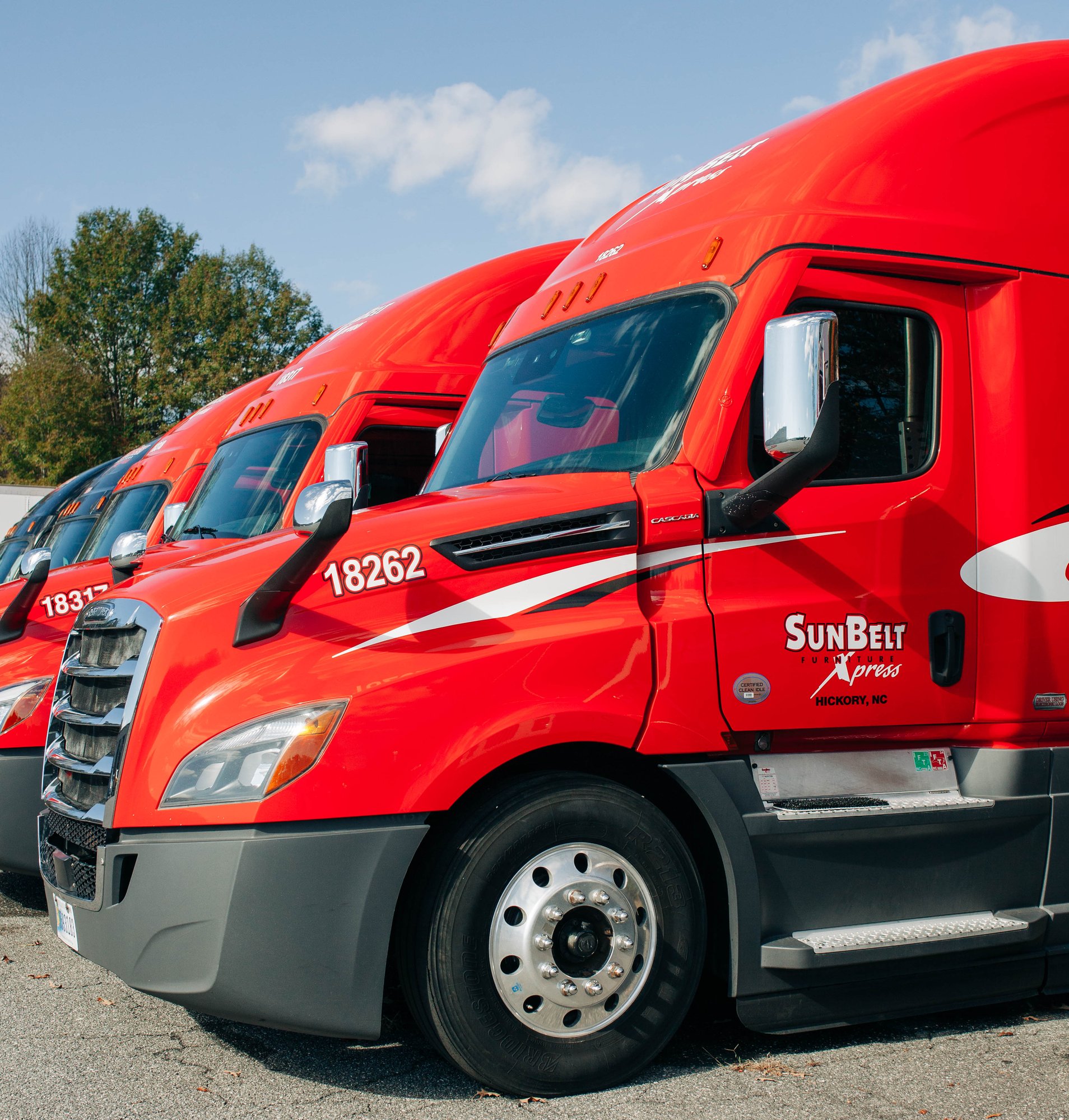 A lineup of red SunBelt Xpress semi trucks, each with a polished finish, parked side by side on a sunny day.