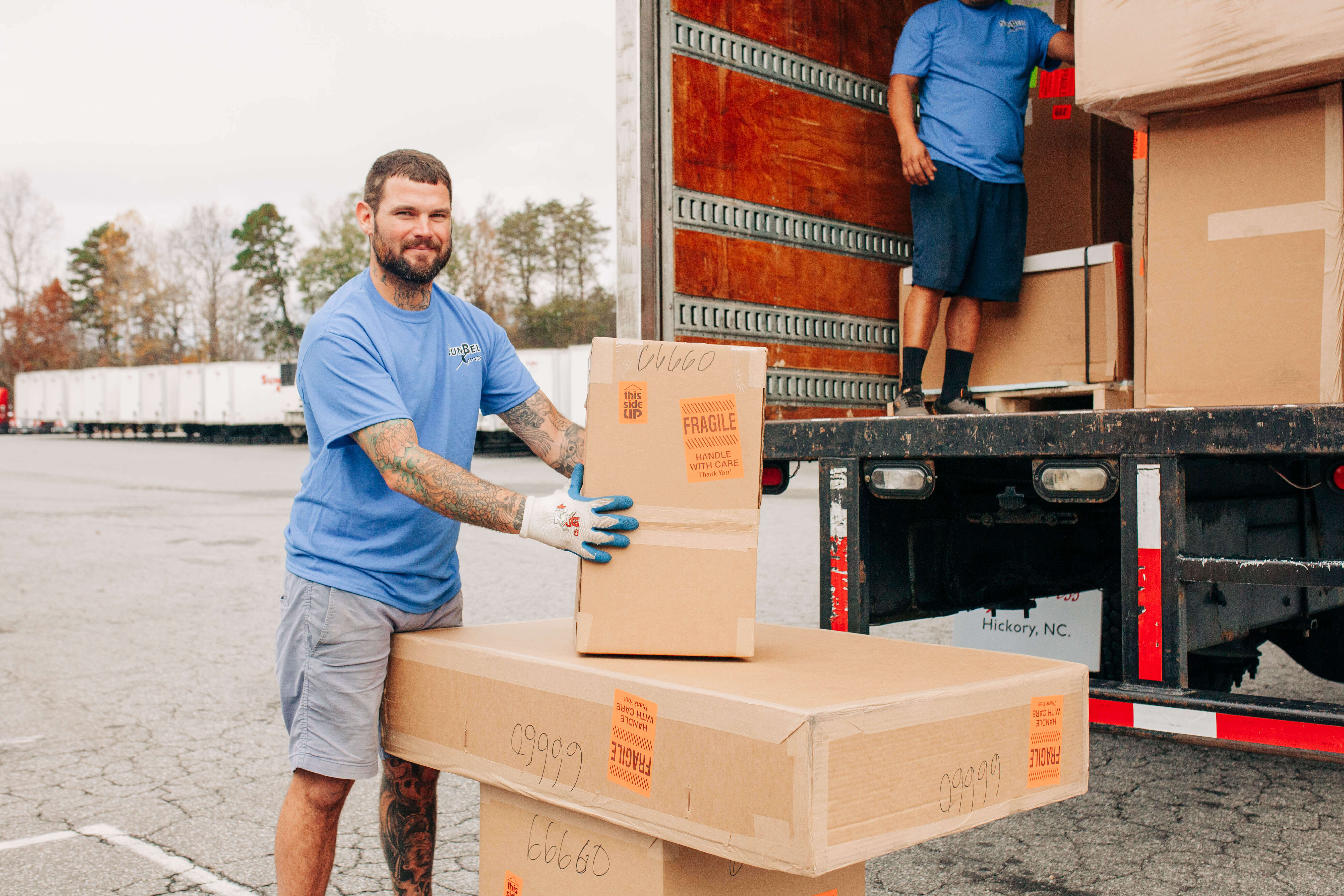 A man in a blue shirt and jeans is holding several boxes, ready to move or deliver them.