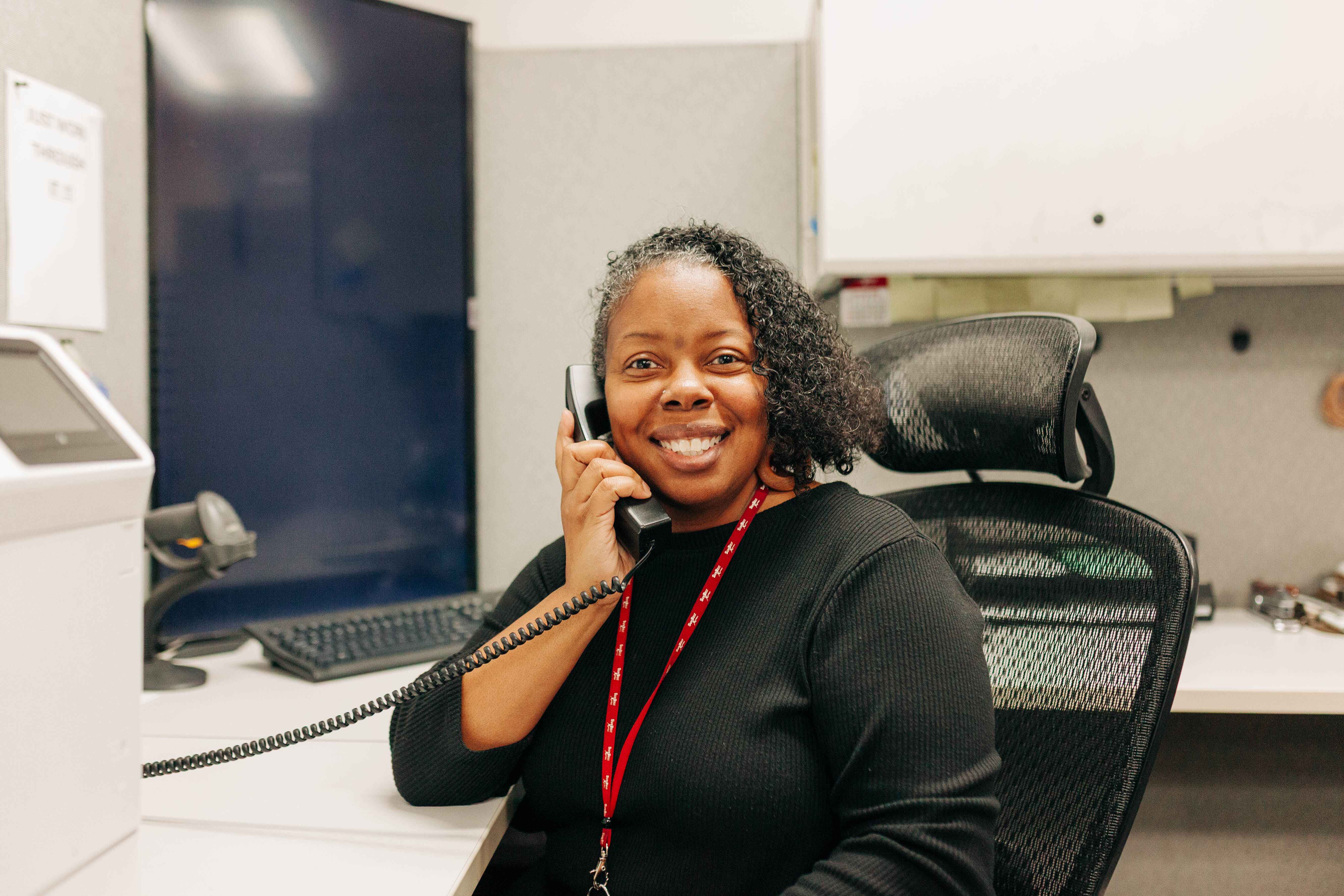 A woman at her desk, talking on the phone with a focused expression.